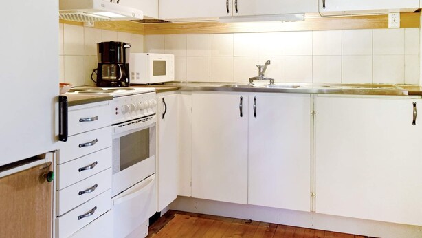 Una cocina con armarios blancos, microondas, cafetera y estufa.