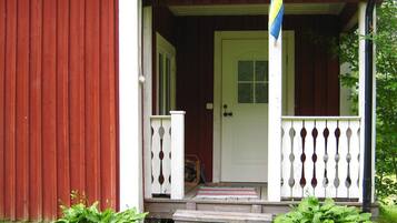 A wooden house with a white door and a porch with a railing.