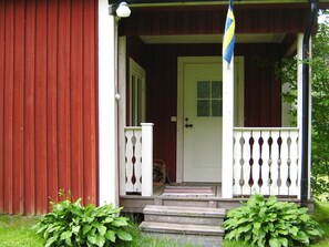 A wooden house with a white door and a porch with a railing. - 7 Person Holiday Home in Sunnemo (Sunnemo)