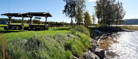A riverside picnic area with a wooden shelter, picnic tables, and a boat on the water.