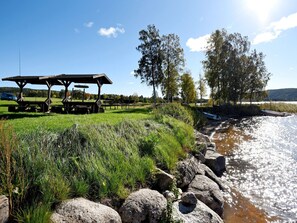 A riverside picnic area with a wooden shelter, picnic tables, and a boat on the water.