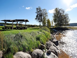 A riverside picnic area with a wooden shelter, picnic tables, and a boat on the water.