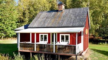 Una casa de madera roja con techo metálico, un porche con barandillas y una chimenea.