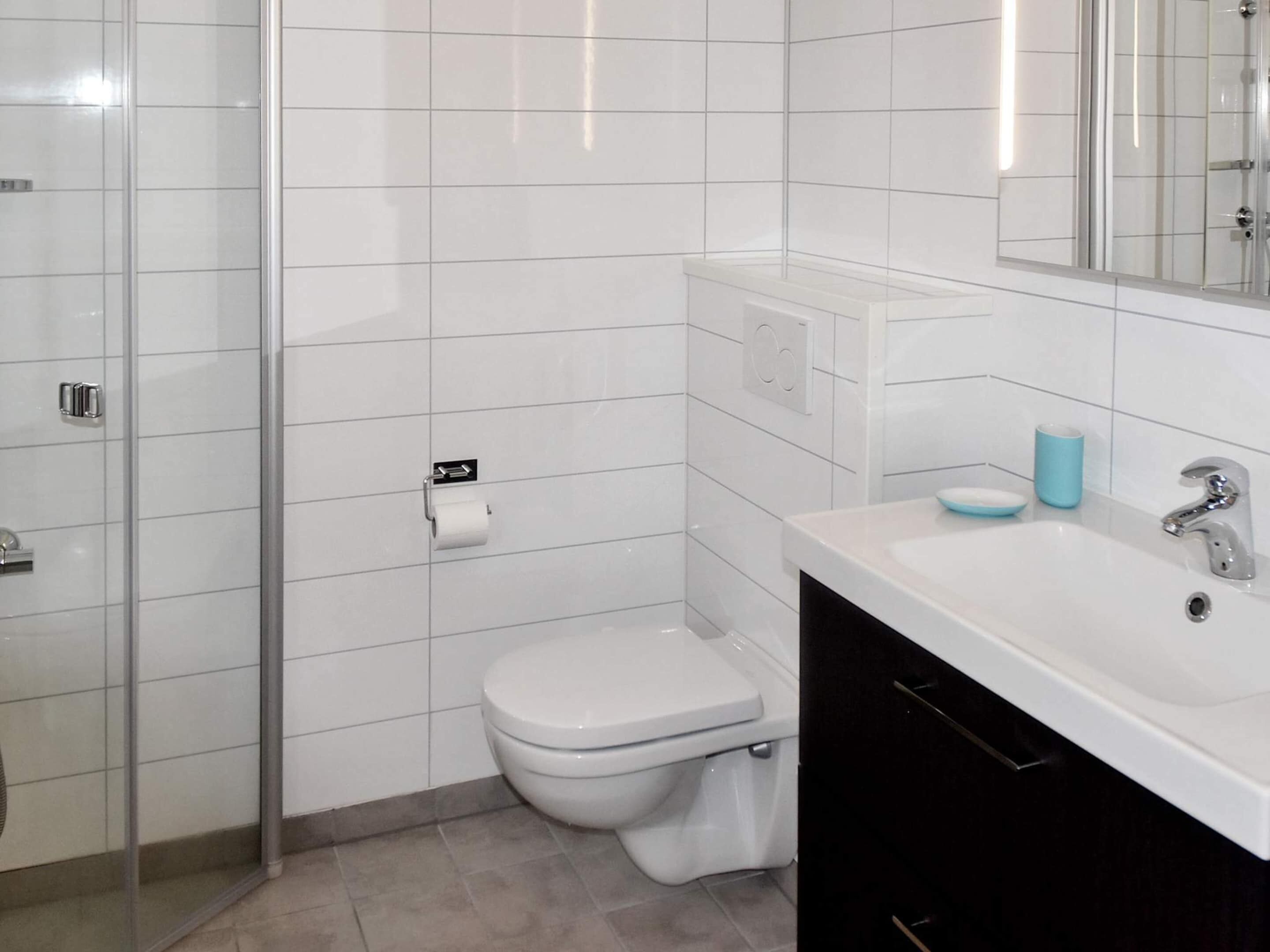 A bathroom with a toilet, a sink, a mirror, and a shower enclosure.