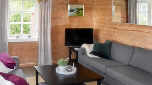 Una sala de estar con un sofá gris, una mesa de centro negra con una planta y un televisor.