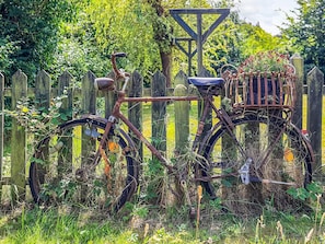 A rusty bicycle with a basket and a metal frame, leaning against a wooden fence in a garden.