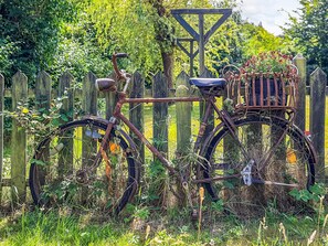 Een roestige fiets met een mandje en een metalen constructie in een tuin.
