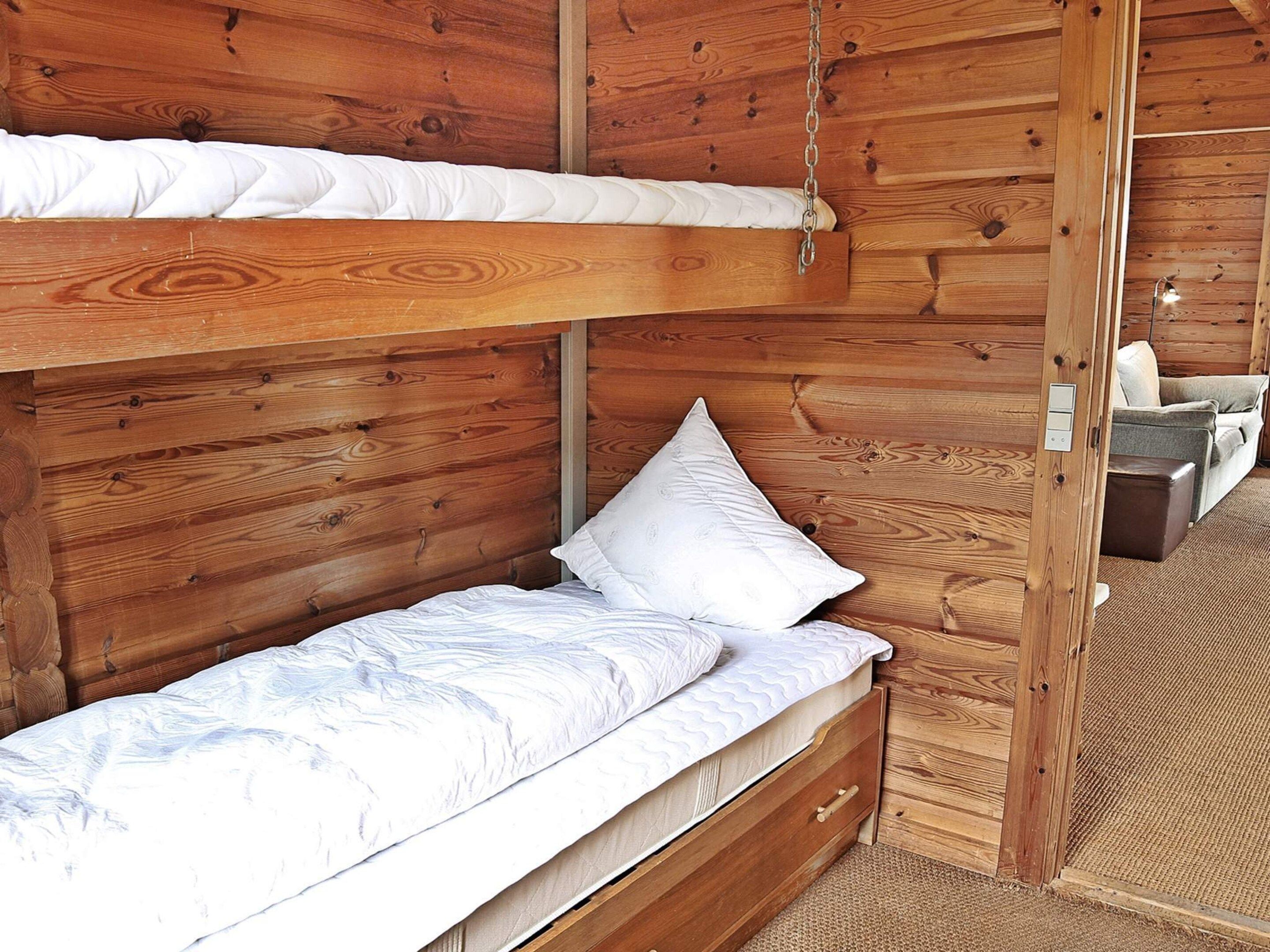 A bunk bed with a mattress and pillows, a wooden dresser, and a small seating area with a cushion and a box.