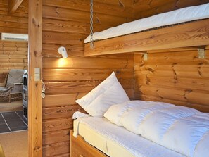 A wooden cabin interior with a bed, a chair, and a wall-mounted light fixture.