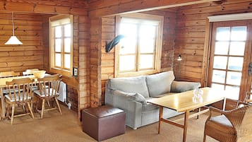 Et interiør af en træhytte med spiseplads, sofa og skammel.