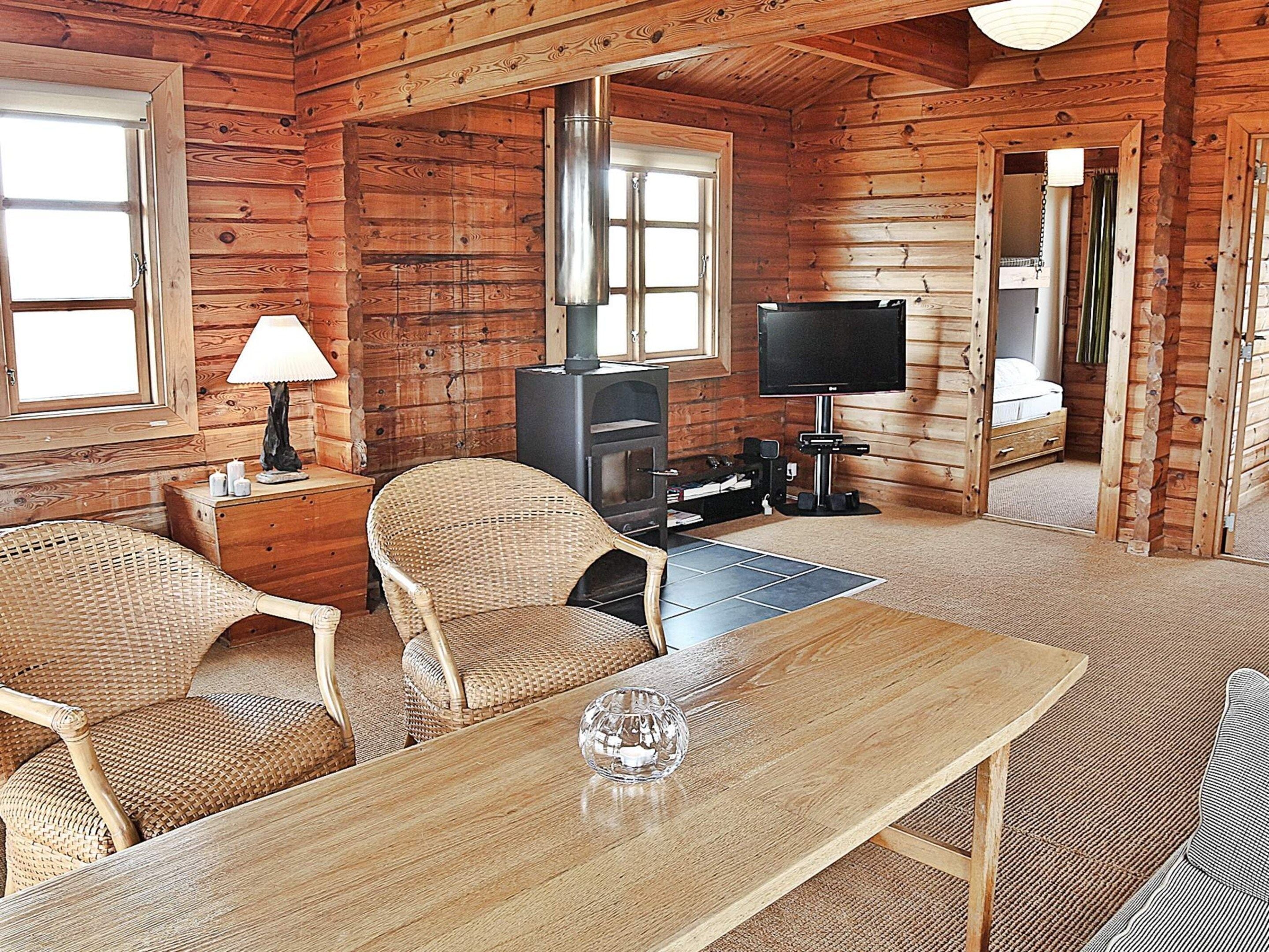 Interior de cabana de toras com sofá, mesa, televisão e lareira.