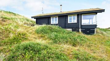 A black wooden cabin with a flat roof, a chimney, and a window on the side.