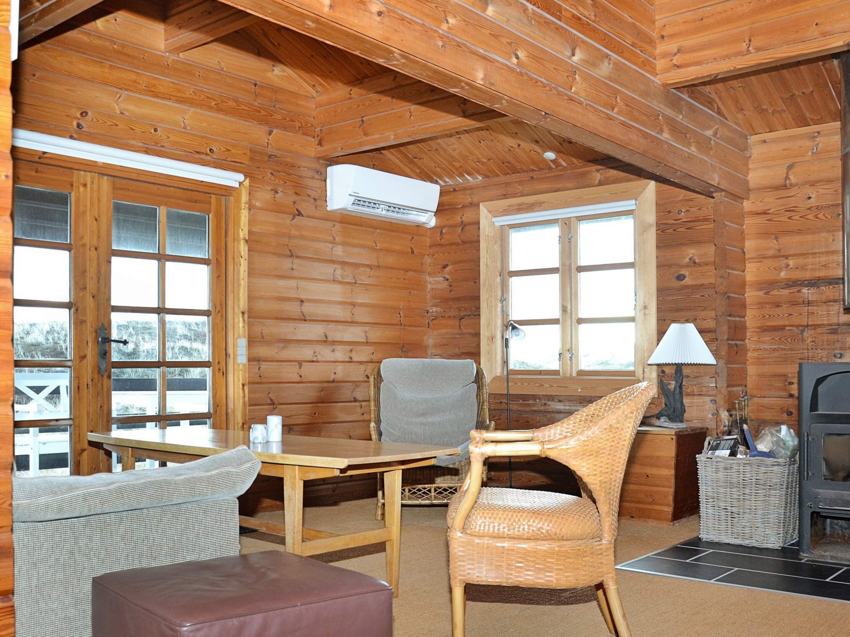 L’intérieur d’un chalet accueillant, avec un plafond en bois, une table entourée de chaises, un canapé, une cheminée et une fenêtre.