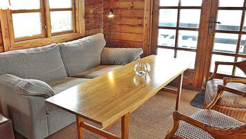 A wooden interior with a sofa, a table, and wicker chairs.