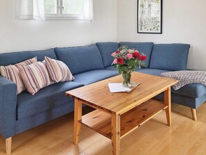 A room with a blue sofa, a wooden coffee table with a vase of flowers, and a framed botanical illustration on the wall.