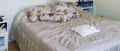 A neatly made bed with floral bedding, a bedside lamp, and a small bedside table with a lamp and a box.
