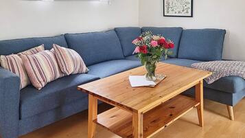 A room with a blue sofa, a wooden coffee table with a vase of flowers, and a framed botanical illustration on the wall.