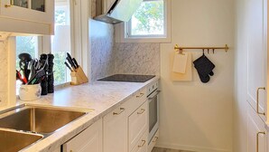 Cocina compacta con muebles blancos, pileta de acero inoxidable y ventana que proporciona luz natural.
