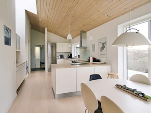 Een moderne keuken met een centraal eiland, een houten plafond en een eethoek met een stenen blikvanger.