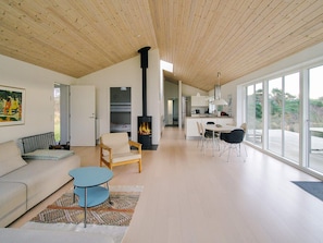 Een moderne woonkamer met een bank, een stoel, een eettafel met stoelen, een open haard en grote ramen met uitzicht op het landschap.