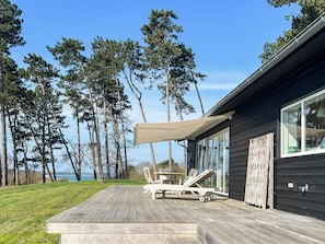 Een houten terras met lounge stoelen en een zonnescherm, met uitzicht op water en bomen.
