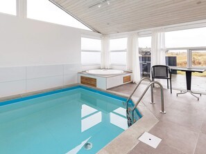 Une piscine intérieure moderne, dotée d’un jacuzzi, d’un patio ensoleillé et offrant une vue sur l’extérieur.