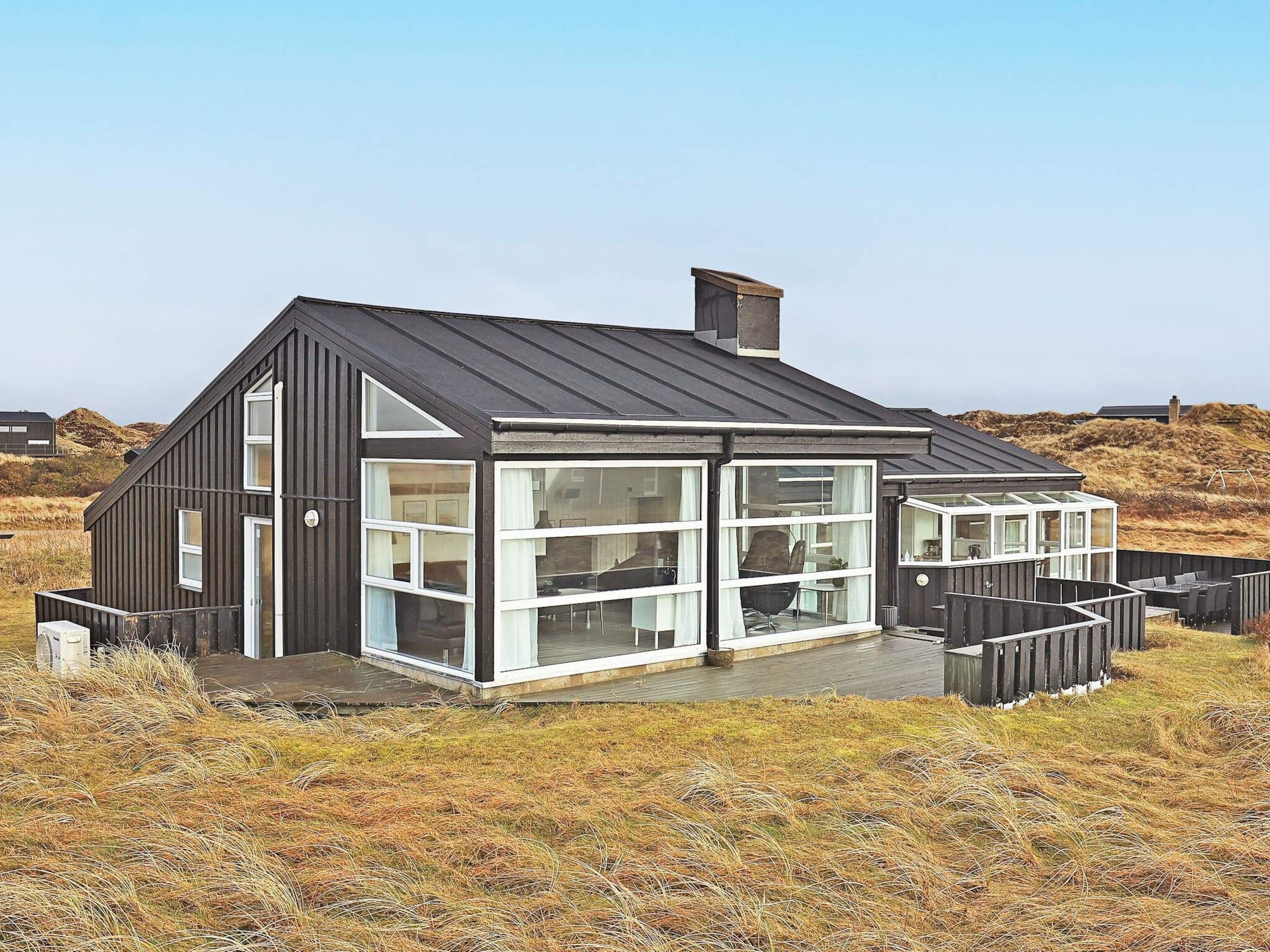 Une maison moderne dotée d’une grande façade en verre, d’une terrasse en bois et d’un toit en métal.