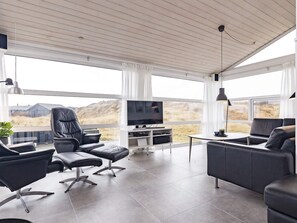 A modern living room with a flat-screen TV, leather sofas, and a large window offering a view of the countryside.