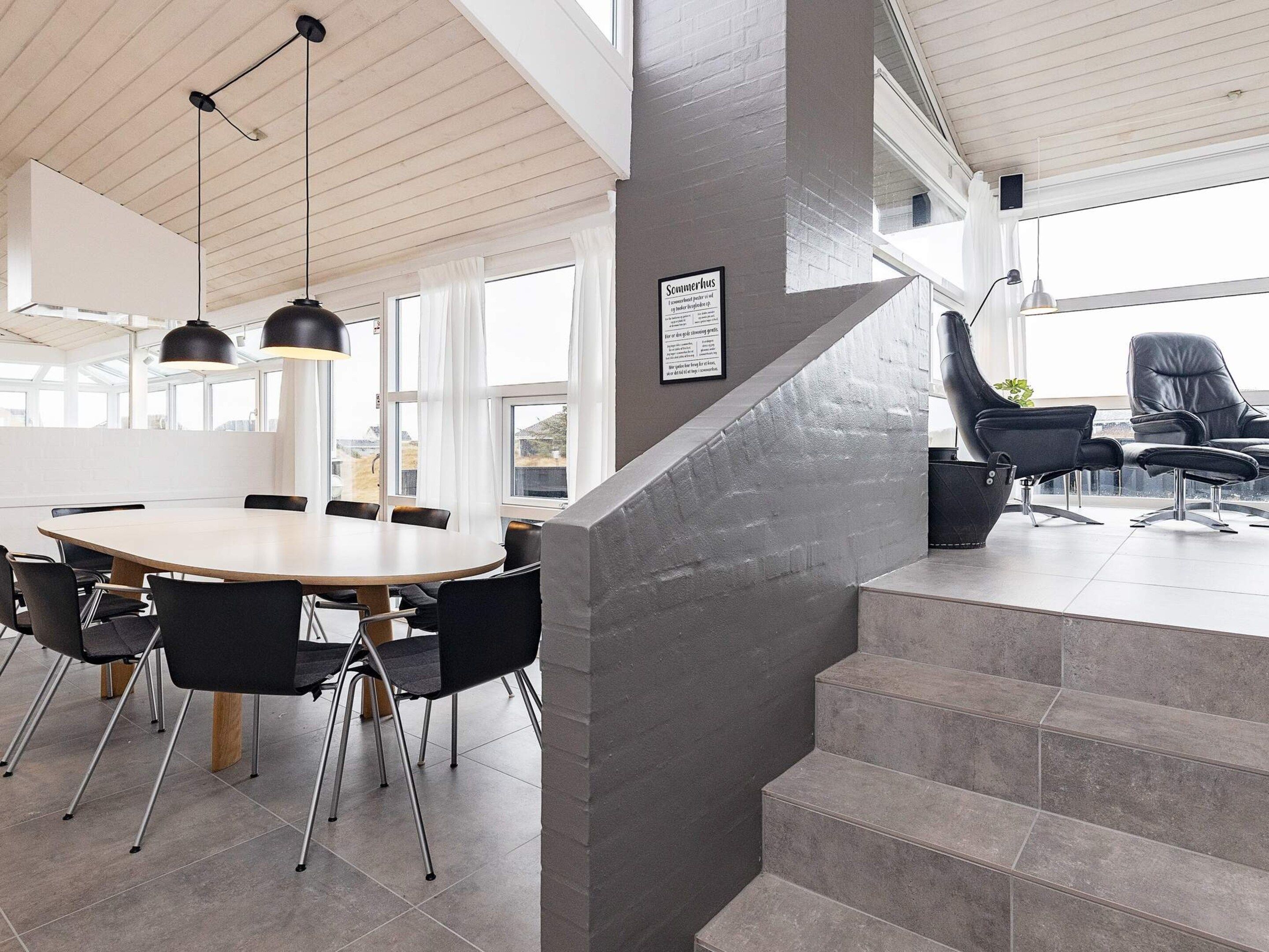 A modern interior with a staircase, a dining area with a round table and chairs, and a seating area with chairs.