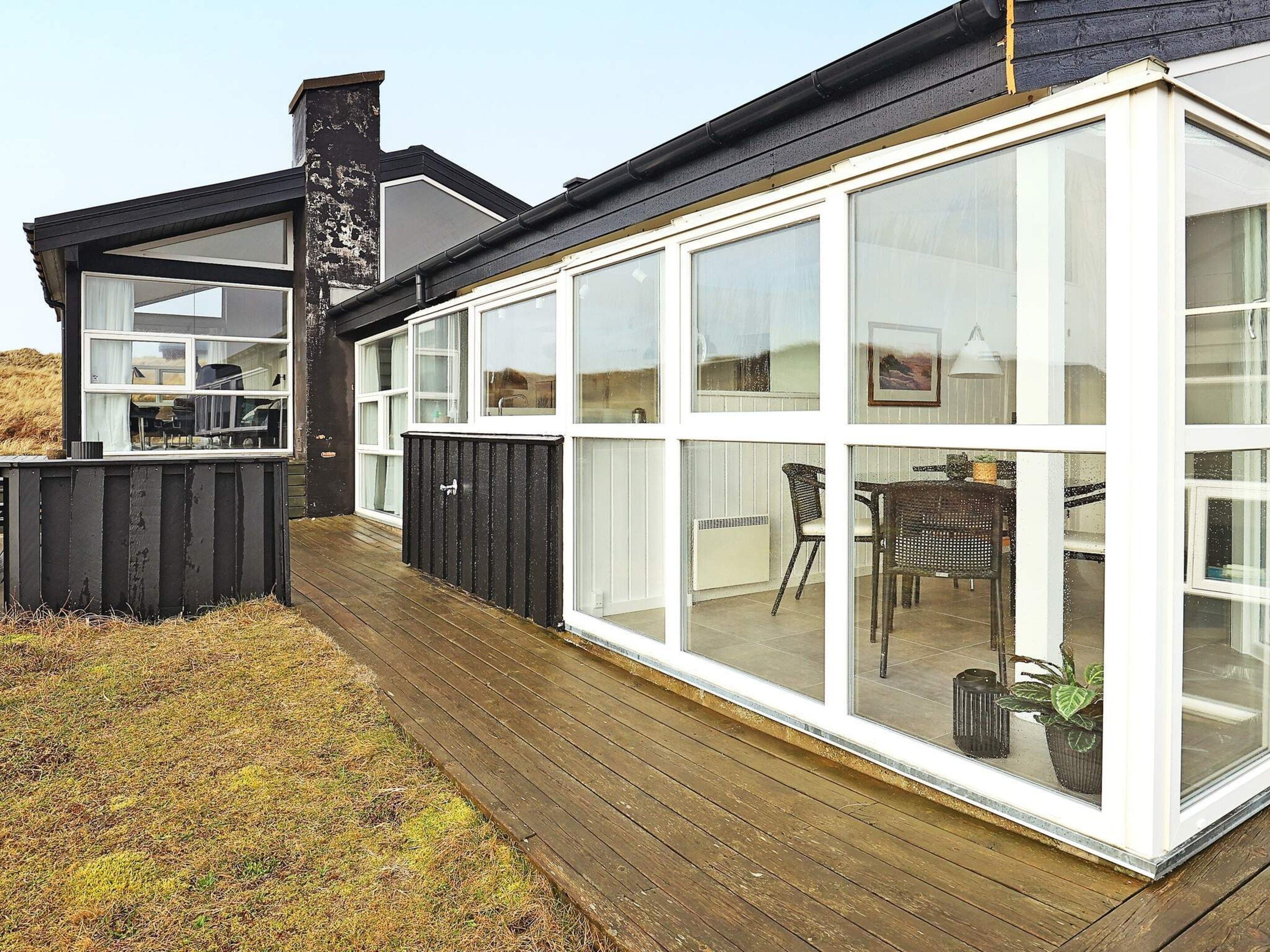 Ein modernes Haus mit großen Fenstern, einer Holterrasse und einer schwarzen Außenfassade.