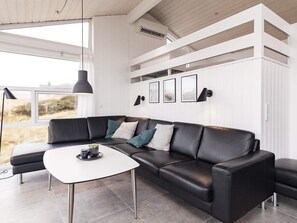 Un salon moderne avec un canapé d’angle en cuir noir, une table basse blanche et une grande fenêtre offrant une vue sur l’extérieur.