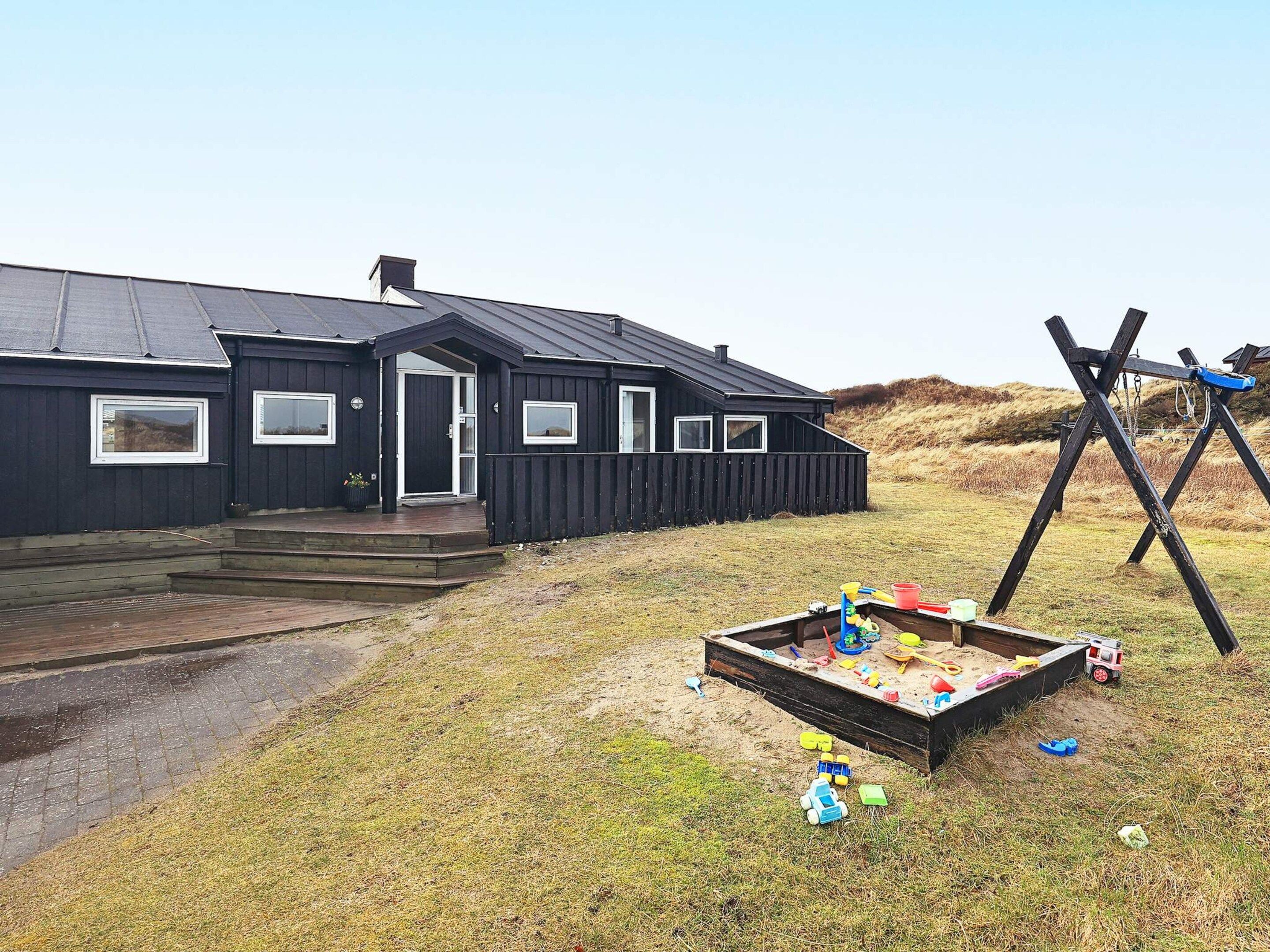 A black building with a porch and a play area with toys.