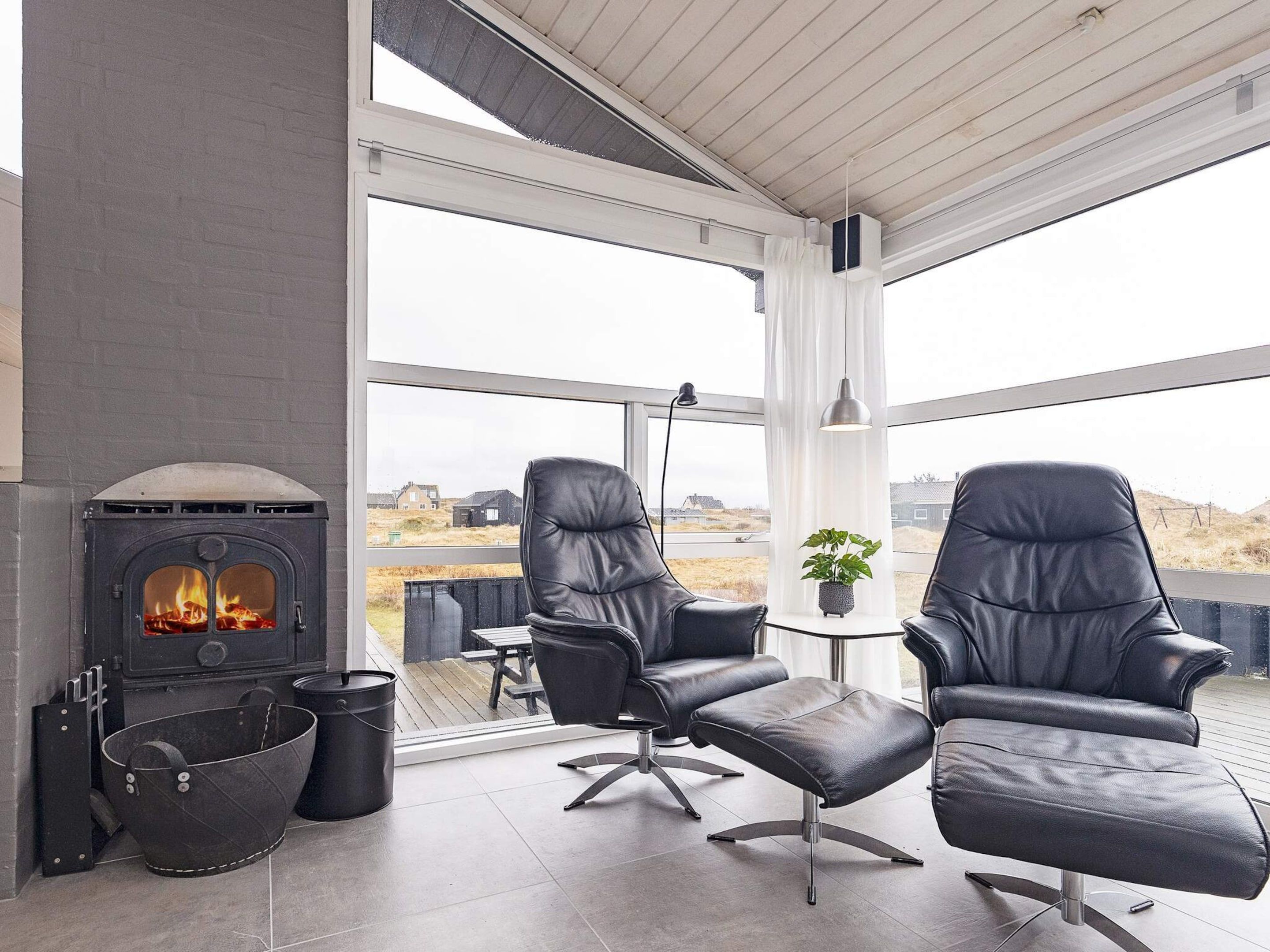 A modern interior with a fireplace, leather chairs, and a view of the outdoors.