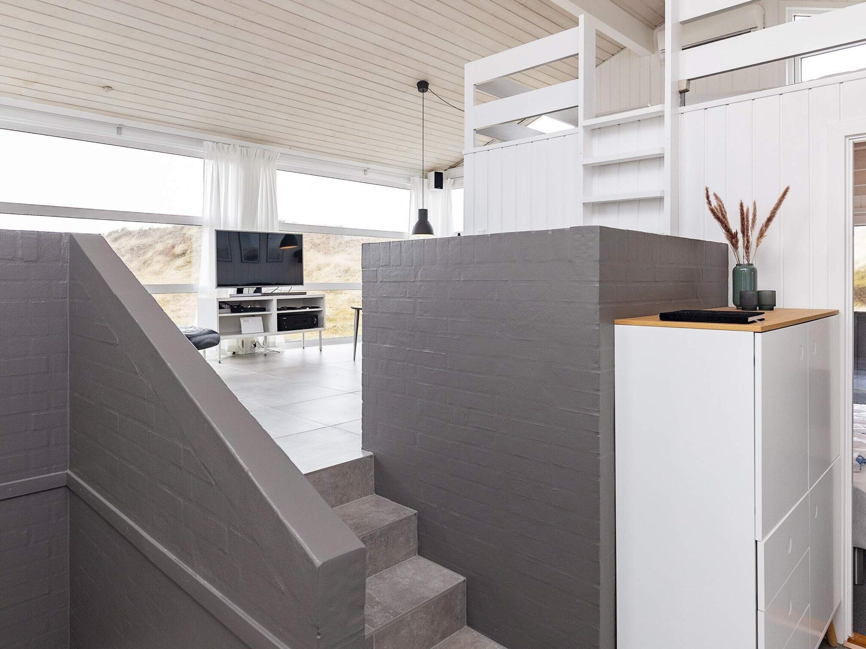 A modern interior with a staircase, a flat-screen TV, and a white cabinet.