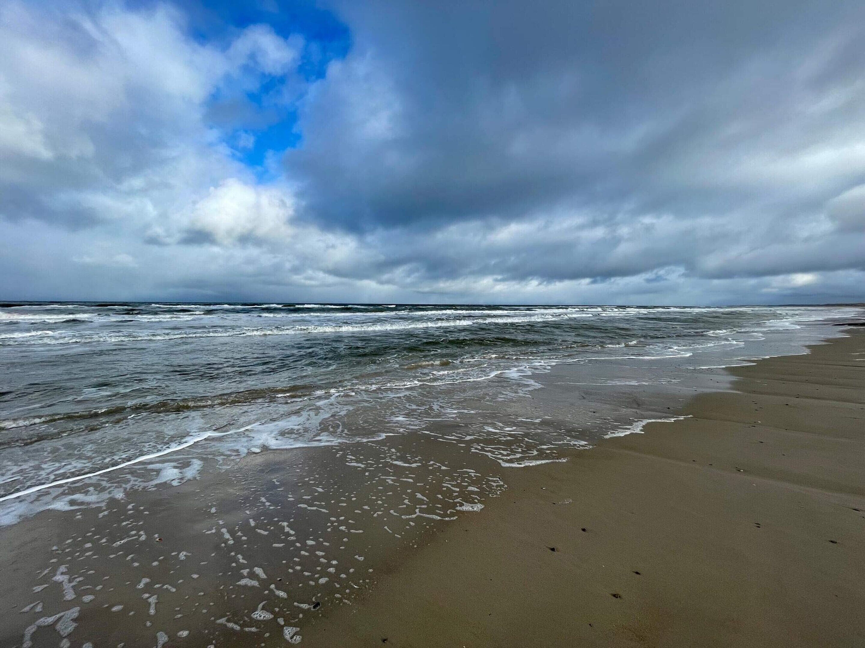 A beach with waves, a cloudy sky, and a sandy shore.