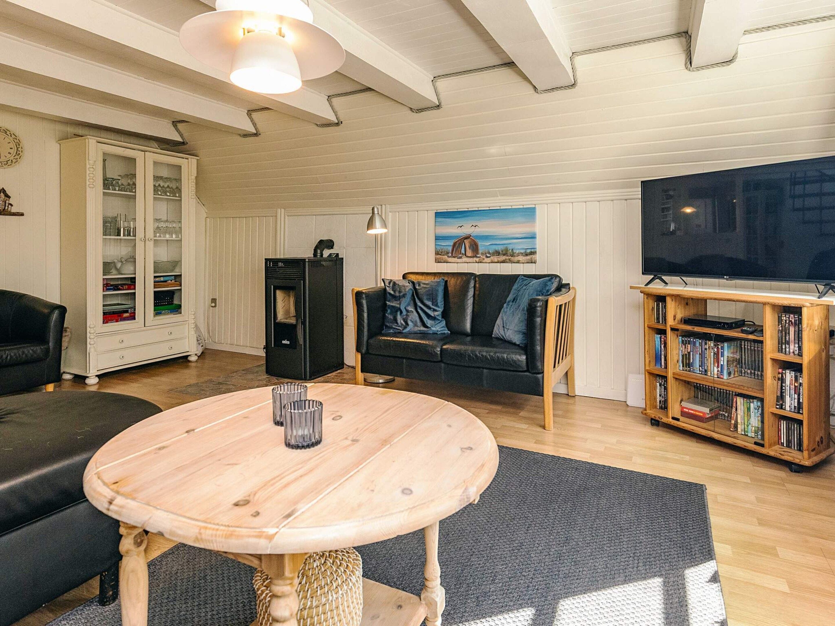 A living room with a wooden table, a black sofa, a television, a bookshelf, and a cabinet with glass doors.