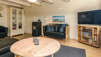 A living room with a wooden table, a black sofa, a television, a bookshelf, and a cabinet with glass doors.