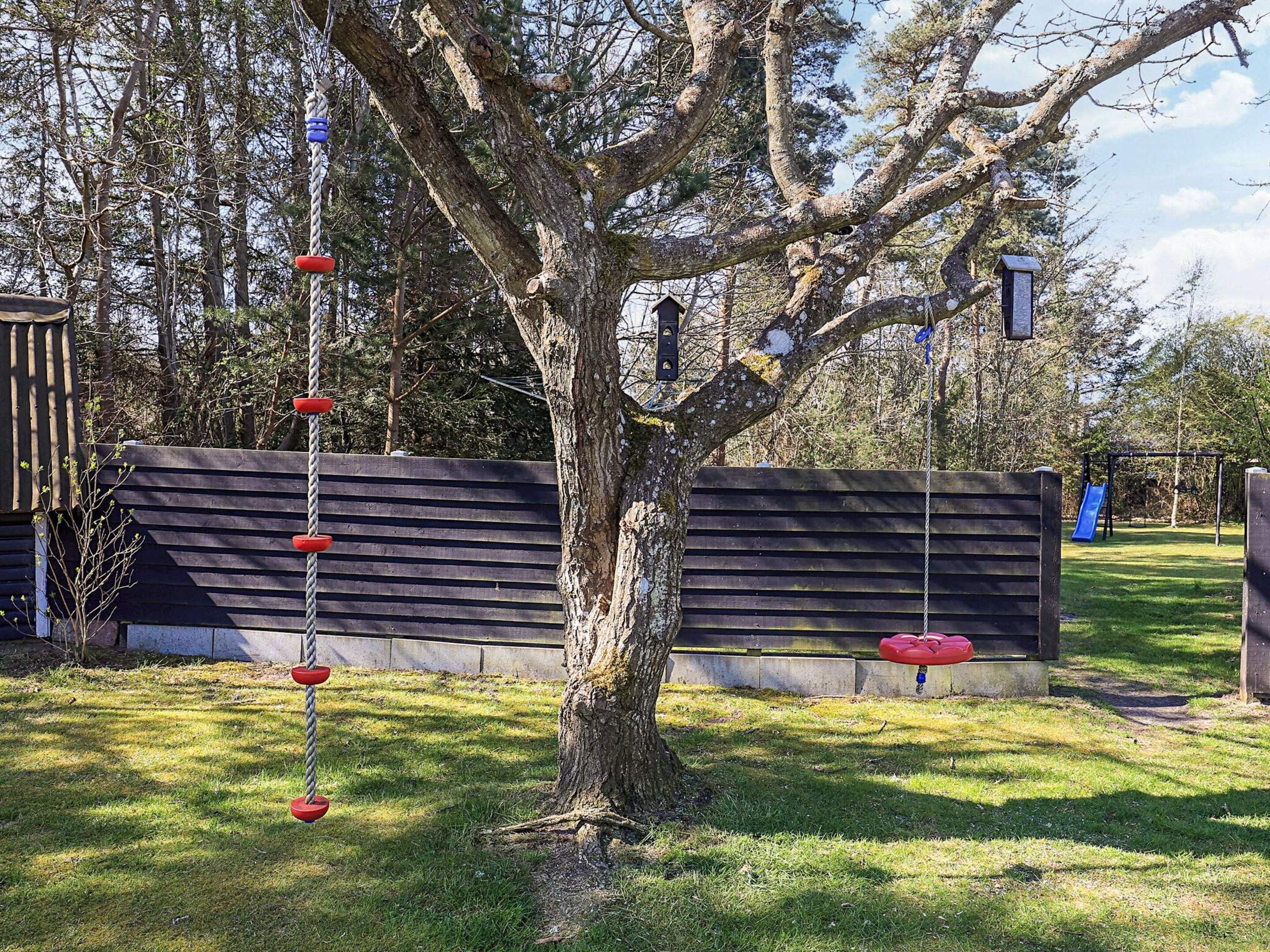 A tree with a swing set and a slide in a park setting.