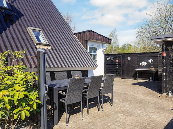 An outdoor patio area with a table and chairs, a black fence, and a building with a corrugated metal roof.