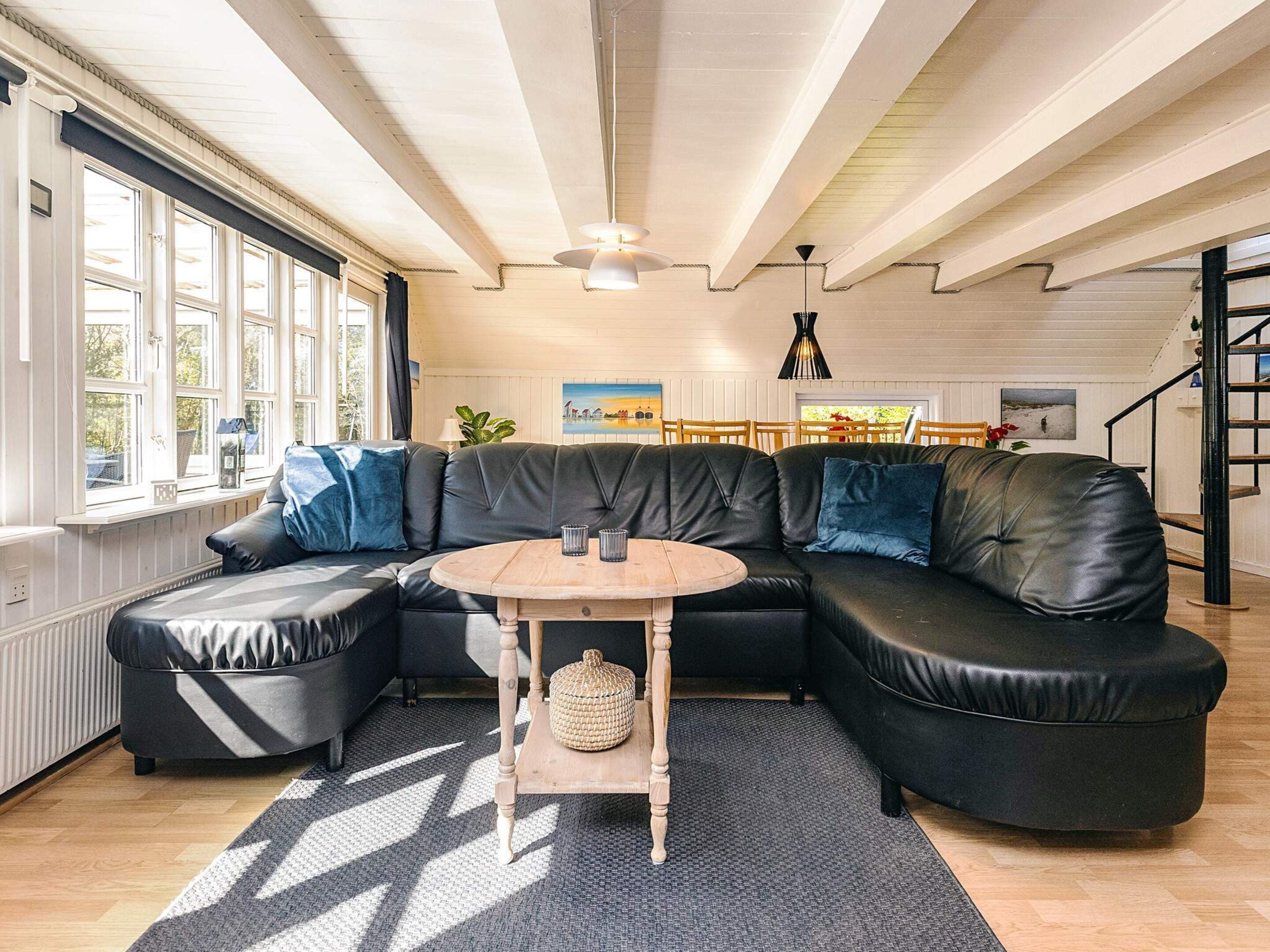 A modern living room with a sectional sofa, a round wooden table, and a staircase.