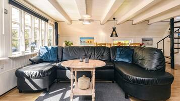Ein modernes Wohnzimmer mit einer Eckcouch, einem runden Holztisch und einer Treppe.