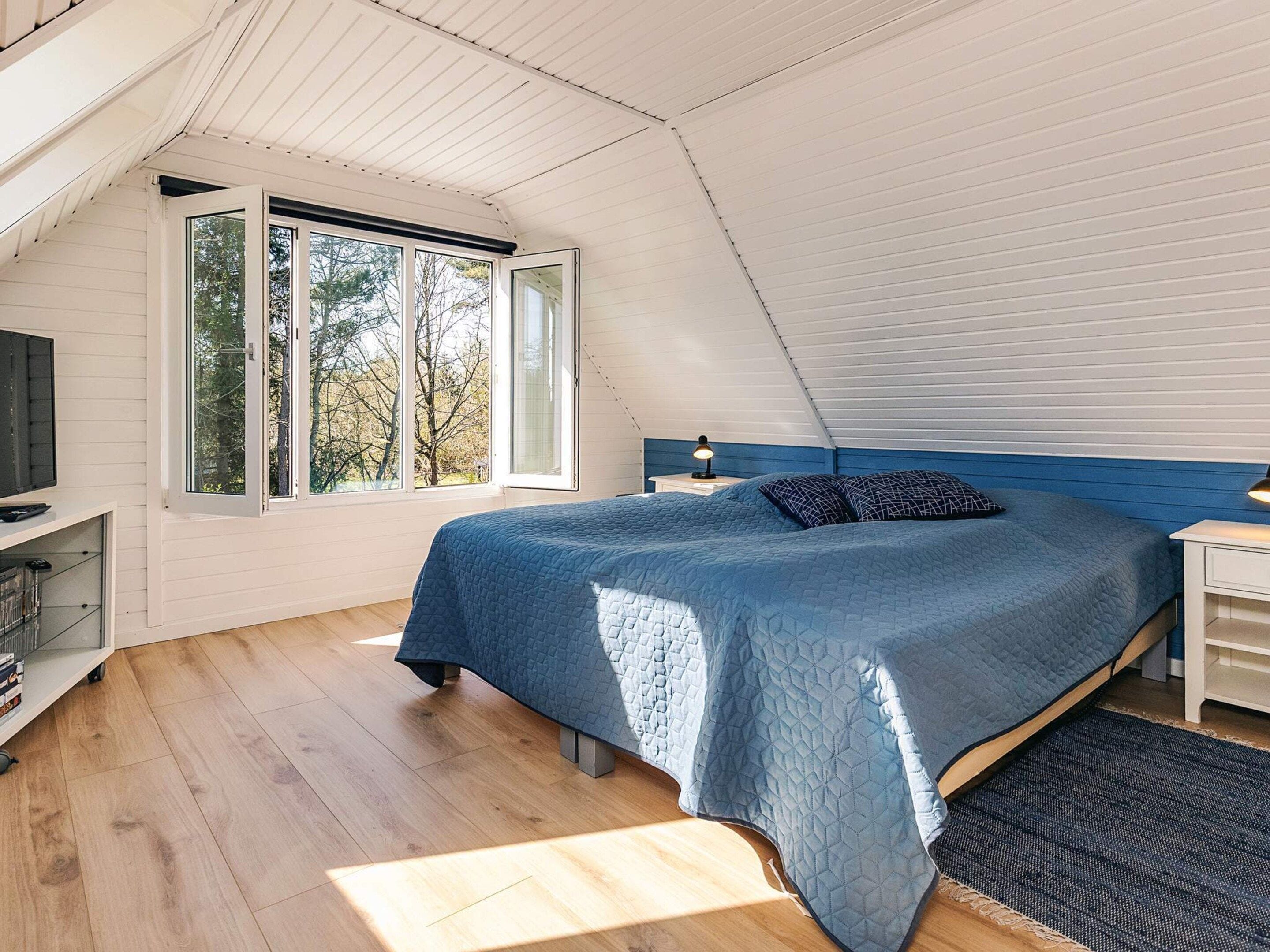 Ein Schlafzimmer mit einem Bett, einem Fernseher, einem Fenster und einem Nachttisch.