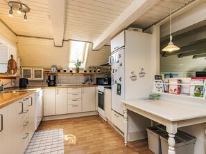 A modern kitchen with wooden cabinets, a white countertop, and a built-in oven. There is a window providing natural light and a hanging light fixture above the counter.