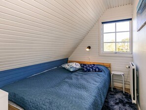 A bedroom with a sloped ceiling, a bed with a blue quilt, a small stool, and a window with a view of trees. - 6 Person Holiday Home in Hals-by Traum (Hals)