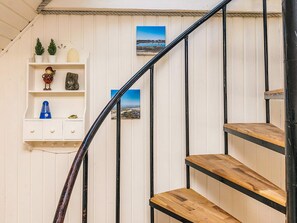 A staircase with wooden steps and black metal railings, leading to a landing with a white wall and a shelf with decorative items.