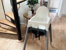 Una silla alta con mesita, una escalera de madera y una planta en maceta.