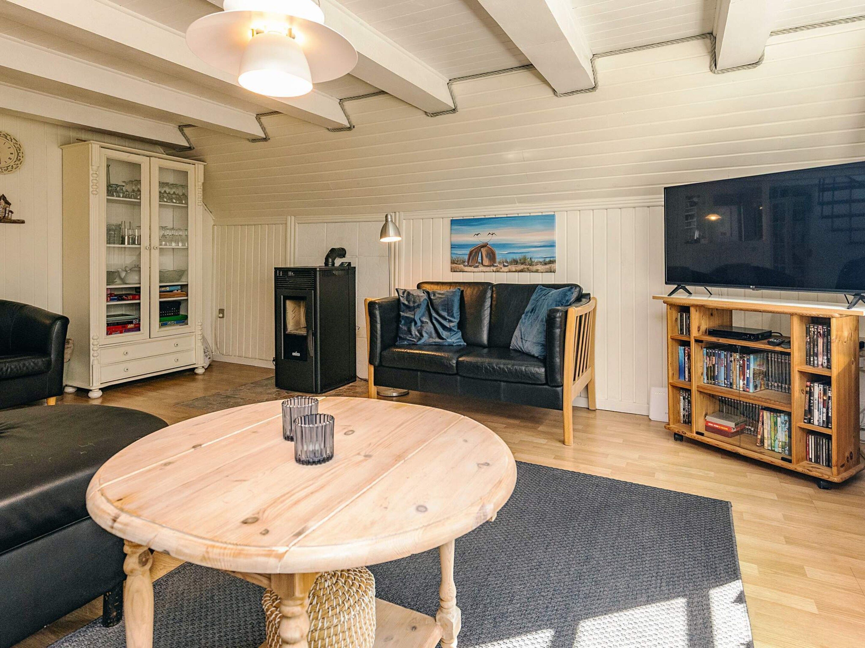 Un salon chaleureux avec une table en bois, un canapé noir, un téléviseur et une bibliothèque.