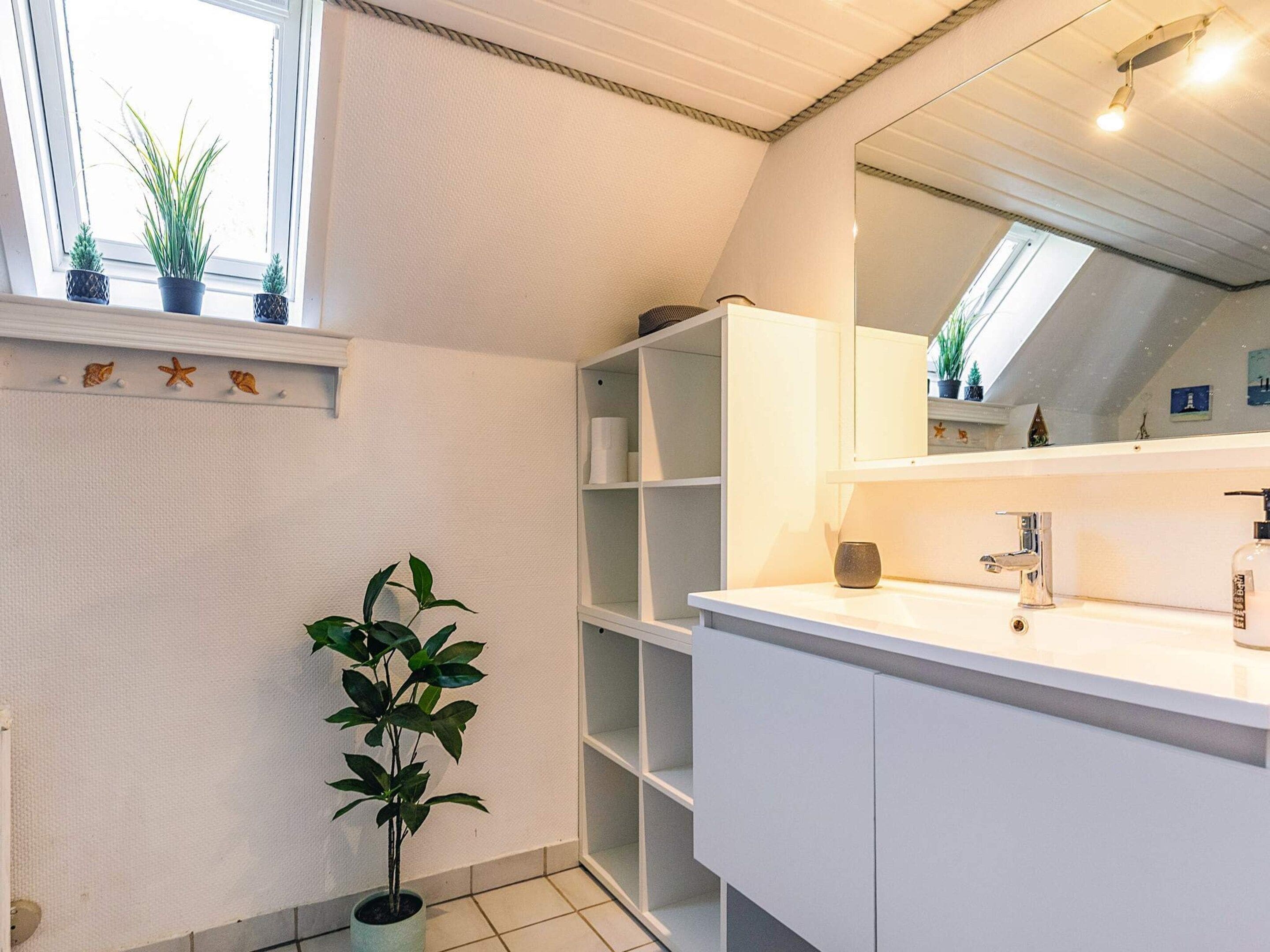 A modern bathroom with a white vanity, a large mirror, and a potted plant.