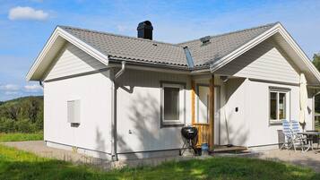 A single-story house with a sloped roof, a chimney, and a small porch with outdoor furniture.