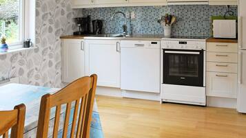 A kitchen with white cabinets, a dishwasher, an oven, and a window with a view of greenery.